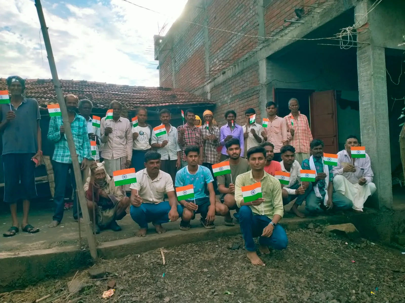 Villagers and young people holding small national flags at a community gathering.